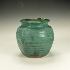 May include: A handcrafted, teal-colored ceramic vase with a textured, ribbed design. The vase has a rounded body and a ruffled rim. The base is a lighter, earthy tone. This decorative piece is suitable for displaying flowers or as a standalone art object.