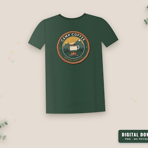 Op de afbeelding: Een donkergroen t-shirt met korte mouwen en een cirkelvormige afbeelding op de borst. Het ontwerp toont bergen, een kampvuur en een koffiemok met de tekst "CAMP COFFEE" en "BREWED OVER FIRE" in een oranje en groene cirkelvormige rand.