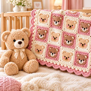 Könnte beinhalten: Ein beigefarbener Plüsch-Teddybär mit einer cremefarbenen Schleife um den Hals sitzt neben einer gehäkelten Babydecke. Die Decke besteht aus einem Gitter aus quadratischen Feldern, die jeweils ein braunes Bärengesicht mit rosa Wangen zeigen.