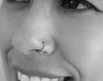 May include: A close-up of a person's face, showing a nose piercing with a small silver hoop. The person is smiling and has their eyes closed.