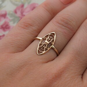 May include: A gold filigree ring with an oval-shaped design. The ring is delicate and intricate, with a floral pattern.