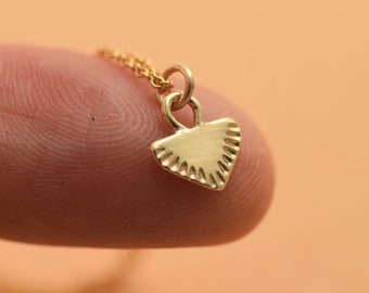 May include: A gold necklace with a small, triangular pendant. The pendant has a textured, fan-like design.