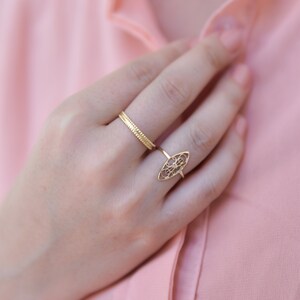 Puede incluir: Primer plano de una mano con dos anillos de oro. El anillo en el dedo &iacute;ndice es una banda delicada, mientras que el anillo en el dedo medio es un dise&ntilde;o m&aacute;s ornamentado con un patr&oacute;n de filigrana.