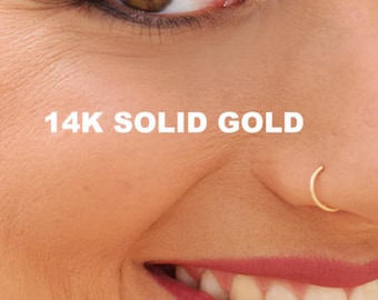 Może przedstawiać: Zbliżenie twarzy osoby z małym złotym kółkiem w nosie. Tekst "14K SOLID GOLD" jest widoczny pod okiem.