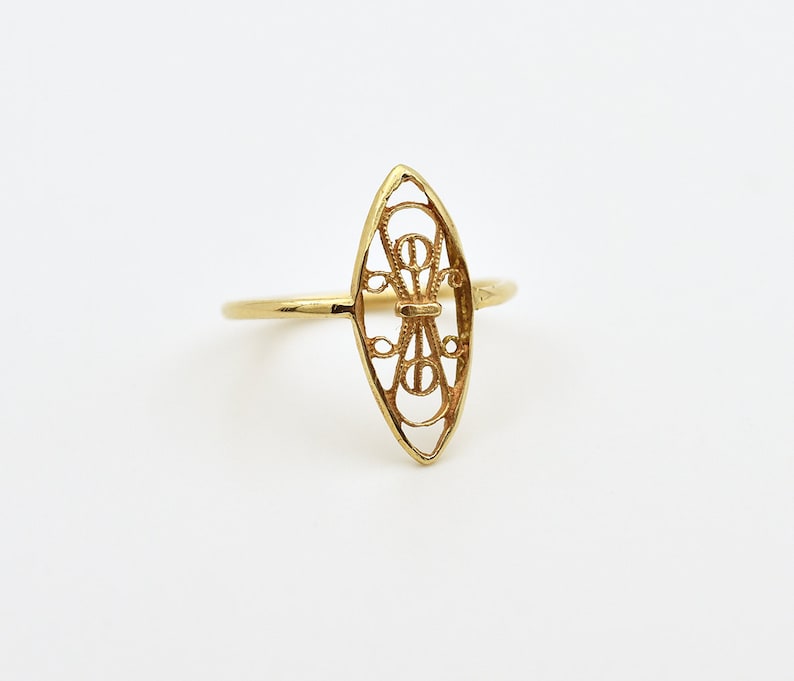 May include: A gold ring with a delicate, openwork design in the shape of an oval. The design features intricate swirls and curves.