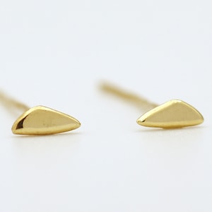 May include: A pair of gold triangle stud earrings. The earrings are small and delicate, and they have a simple, minimalist design.