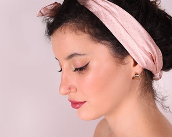 May include: A woman with dark curly hair wearing a pink polka dot headband and gold hoop earrings. She is wearing a nose ring.