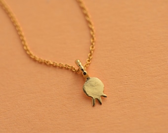 May include: A gold chain necklace with a small, gold, pomegranate-shaped pendant.