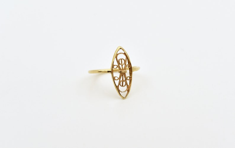Puede incluir: Un anillo de filigrana dorada con un dise&ntilde;o en forma de diamante. El anillo es delicado e intrincado.