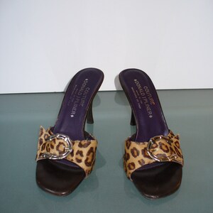 Puede incluir: Un par de sandalias de tac&oacute;n Donald J Pliner Couture. Los zapatos de punta abierta presentan una suela de cuero marr&oacute;n, una correa con estampado de leopardo con hebilla plateada y una plantilla morada oscura. Los tacones miden unos 10 cm.