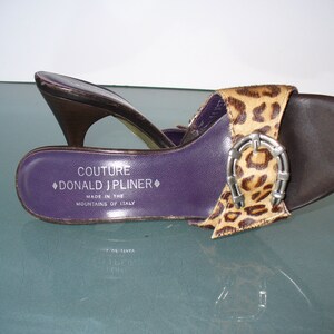 Puede incluir: Sandalia abierta marr&oacute;n y con estampado de leopardo con hebilla plateada. La sandalia tiene una plantilla morada con el texto "COUTURE DONALD J PLINER MADE IN THE MOUNTAINS OF ITALY". El tac&oacute;n es marr&oacute;n oscuro.