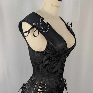 May include: A black corset with a paisley pattern and lace-up details. The corset has a deep V-neckline and is sleeveless. It is made of a satin-like fabric and has a boned structure.