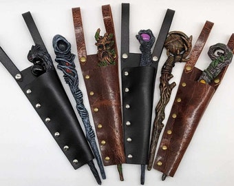 May include: A collection of fantasy wands with detailed, sculpted tops, each housed in a leather sheath. The wands feature various designs, including a wolf, a hooded figure, a tree spirit, and a claw. The sheaths are black and brown, with riveted accents.