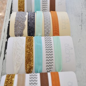 May include: A set of 10 colorful hair ties with different patterns, including glitter, lace, chevron, and polka dots. The hair ties are arranged on a white background with the word "aloha" printed on each card.