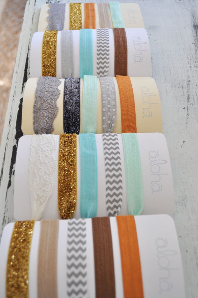 May include: A set of 10 colorful hair ties with different patterns, including glitter, lace, chevron, and polka dots. The hair ties are arranged on a white background with the word "aloha" printed on each card.