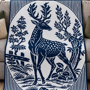 May include: A rectangular throw blanket featuring a dark blue and white color scheme. The center displays a detailed deer standing within an oval frame, surrounded by trees and foliage. The border consists of vertical blue and white stripes.