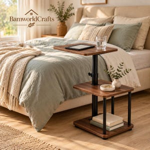 May include: A two-tier side table with a dark wood grain finish and black metal frame. The adjustable top shelf holds a tablet and a glass of water, while the lower shelf holds a small white bowl and two stacked books.