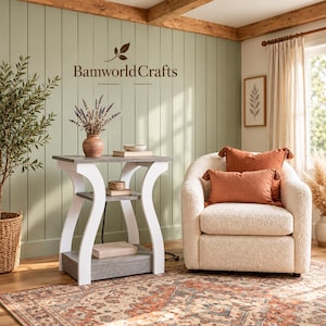 May include: A three-tier side table with white curved legs and gray wood-grain shelves, featuring the text Bamworld Crafts on the wall above. The table holds a vase of dried lavender and books, positioned next to a cream-colored textured armchair.