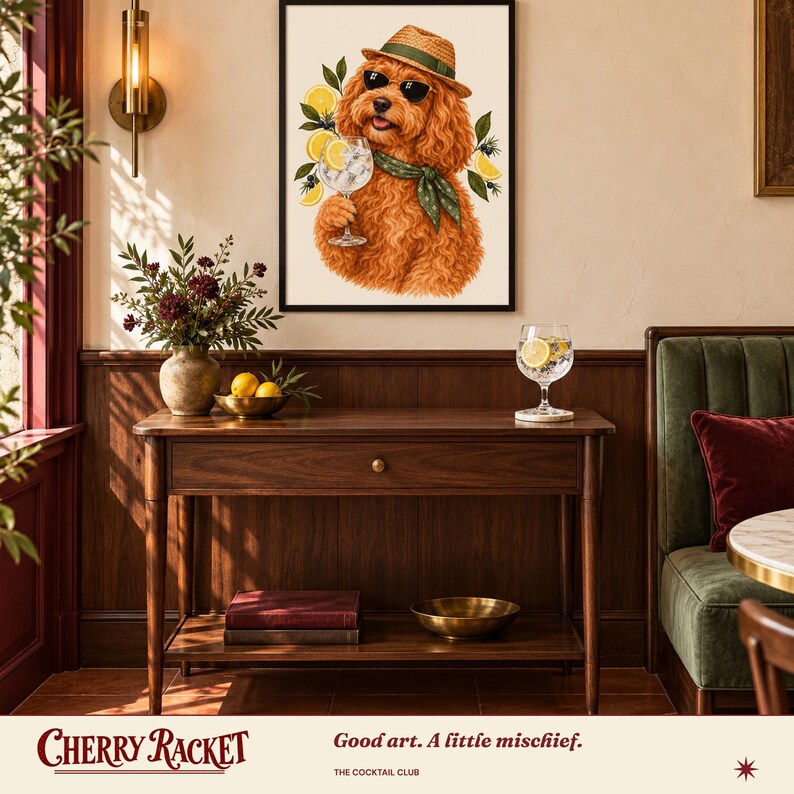 May include: A framed wall art print featuring a fluffy ginger dog wearing a straw hat, sunglasses, and a green scarf, holding a glass of gin and tonic garnished with lemon slices and green leaves against a cream background.