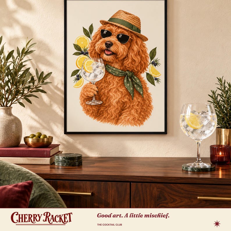 May include: A framed wall art print featuring a fluffy ginger dog wearing a straw hat, sunglasses, and a green patterned neckerchief. The dog holds a glass of gin and tonic garnished with lemon slices and juniper berries against a cream background.