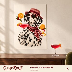 May include: A wall art print featuring a Dalmatian dog wearing a red fedora, red sunglasses, and a red paisley bandana. The dog holds a pink cocktail glass, surrounded by orange slices and cherries. The text reads Cherry Racket.