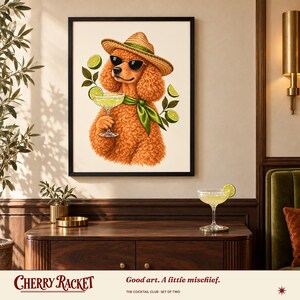 May include: A framed wall art print featuring a curly orange poodle wearing a straw hat, black sunglasses, and a green neck scarf. The poodle holds a margarita glass, surrounded by floating lime slices on a cream-colored background.