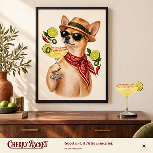 Op de afbeelding: Een ingelijste kunstdruk van een beige chihuahua met een strooien hoed, zwarte zonnebril en een rode bandana met paisley-motief. De hond houdt een margaritaglas met een zoutrand vast, omringd door zwevende limoenschijfjes, jalape&ntilde;o en rode pepers.
