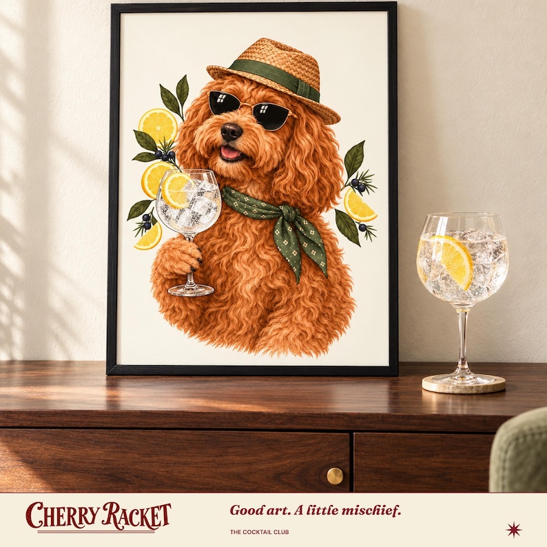 May include: A framed wall art print featuring a curly-haired ginger dog wearing a straw fedora, dark sunglasses, and a green patterned neckerchief. The dog holds a glass filled with ice and a lemon slice, surrounded by lemon slices and green leaves.