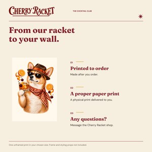 May include: A wall art print featuring a dog wearing a brown fedora, sunglasses, and a red paisley bandana, holding a cocktail glass with orange slices and cherries. The text reads Cherry Racket, The Cocktail Club, and From our racket to your wall.