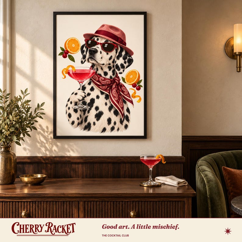 May include: A framed wall art print featuring a Dalmatian dog wearing a red fedora, red sunglasses, and a red paisley bandana. The dog holds a pink cocktail glass, surrounded by floating orange slices and cherries on a cream background.
