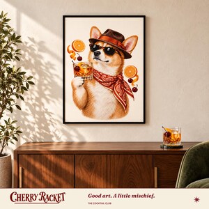 May include: A framed wall art print featuring a tan and white Corgi wearing a brown fedora, black sunglasses, and a red paisley bandana. The dog holds a glass of amber liquid with orange slices and cherries floating around it.