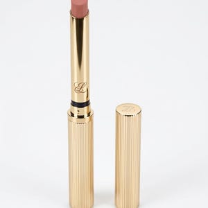 Könnte beinhalten: Ein schlanker Lippenstift in einem Altrosa-Farbton in einer zylindrischen goldfarbenen Metallhülse mit vertikalen Rillen. Die Hülse zeigt einen kleinen eingravierten Buchstaben B auf der Basis und der Kappe, mit einem glatten goldenen Hals.