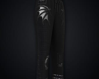 May include: Black sweatpants featuring a subtle grid pattern, an elastic drawstring waistband, and a graphic of a dragon wing on the upper thigh. A small rectangular patch with text is visible near the waist, and a dotted panel is on the lower leg.