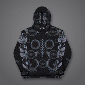 Puede incluir: Una sudadera negra con capucha y manga larga que presenta un estampado integral de motivos oculares circulares grises, s&iacute;mbolos alados y un dise&ntilde;o central de columna vertebral vertical. La sudadera incluye un bolsillo canguro y cordones blancos.