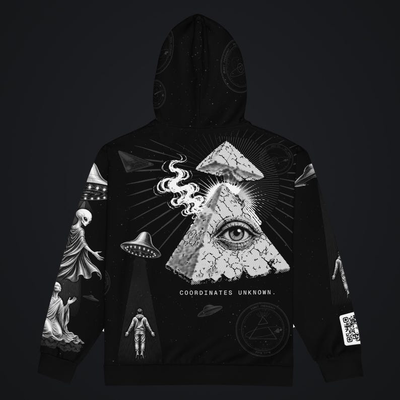 May include: A black hoodie featuring a graphic print of a cracked pyramid with an eye, smoke, and UFOs. The design includes a person standing in a light beam, celestial elements, and the text "COORDINATES UNKNOWN." A QR code is visible on the sleeve.