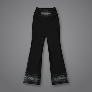 Pu&ograve; includere: Pantaloni neri a vita alta con gamba svasata, caratterizzati da un dettagliato motivo geometrico simmetrico bianco e grigio centrato sulla vita e lungo l'orlo inferiore di ogni gamba, in netto contrasto con il tessuto nero.