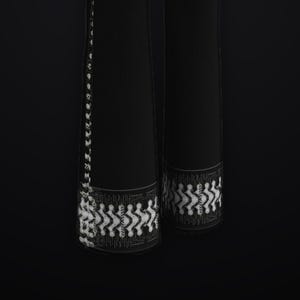 May include: A pair of black trousers featuring a white graphic circuit board pattern along the outer side seams and a horizontal band of the same white digital-style design at the bottom hem of each pant leg against a solid black background.