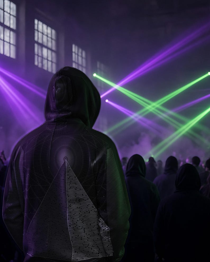 May include: A black hooded sweatshirt featuring a geometric pyramid graphic on the back, worn by an individual standing in a dark room illuminated by bright purple and green laser light beams that cut through the hazy atmosphere.