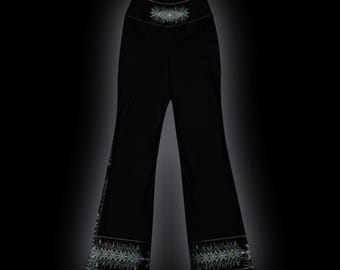 May include: Black high-waisted pants featuring a wide-leg silhouette. The waistband and the lower hem of each leg are decorated with a detailed, symmetrical white and light green graphic pattern that resembles a stylized botanical design.