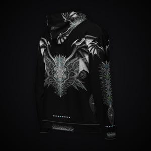 May include: A black hoodie featuring a white graphic print of stylized wings and geometric patterns on the back and hood. The sleeve displays a vertical column of intricate symbols, while a row of small dots is printed above the bottom hem.