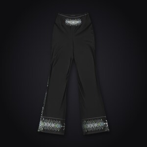 Pu&ograve; includere: Pantaloni neri a vita alta caratterizzati da una stampa grafica simmetrica bianca e verde acqua al centro della vita e lungo l'orlo inferiore di ogni gamba. I pantaloni presentano un taglio a gamba dritta e un tessuto nero liscio.