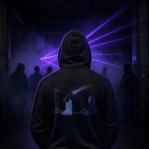 May include: A black hooded sweatshirt featuring a graphic on the back of a person in a white dress standing on a rooftop at night, looking at a shooting star near a water tower and antenna, set against a dark background with purple light beams.