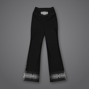 May include: Black high-waisted pants featuring a white geometric pattern at the hem and a matching white decorative emblem centered on the waistband. The pants have a flared leg silhouette with a solid black finish throughout the main body.
