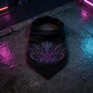 May include: A black triangular bandana featuring a central purple and teal geometric graphic. The design includes a complex star-like pattern surrounded by abstract flowing lines and small text elements in a vibrant neon color palette.