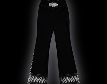 May include: Black high-waisted pants featuring a white geometric pattern at the waistband and a matching white decorative border along the bottom hem of each pant leg. The pants have a straight-leg cut and a solid black fabric construction.