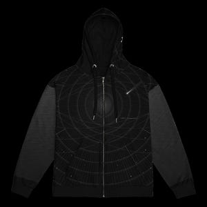 May include: A black zip-up hoodie featuring a white graphic print of concentric circular lines and a shooting star. The design includes a central dark sphere and small scattered dots. The sleeves have a subtle horizontal line pattern.