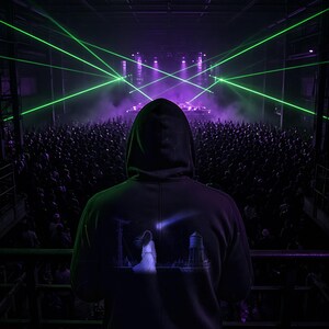 May include: A black hooded sweatshirt featuring a graphic print on the back. The print depicts a figure standing before a water tower and utility pole under a shooting star. The garment is worn in a dark venue with green laser lights.
