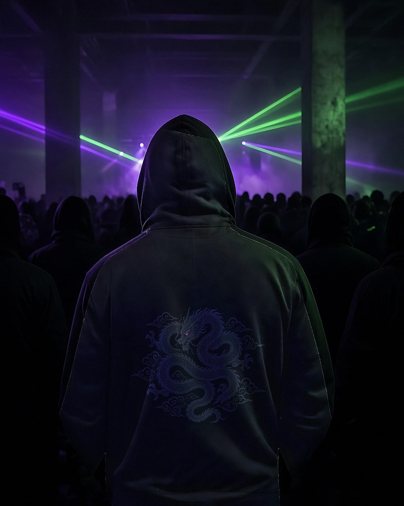 Puede incluir: Una sudadera con capucha de color oscuro que presenta un gr&aacute;fico detallado de un drag&oacute;n enroscado en la espalda. El dise&ntilde;o del drag&oacute;n est&aacute; representado en tonos violeta claro, sobre un fondo de un espacio interior oscuro y concurrido con l&aacute;seres.