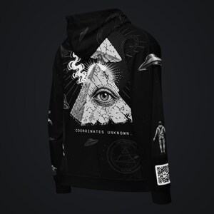 May include: A black hoodie featuring a white graphic of an eye inside a cracked pyramid, with smoke, UFOs, and a floating figure. The text "COORDINATES UNKNOWN." is printed below the pyramid, and a QR code is visible on the lower sleeve.