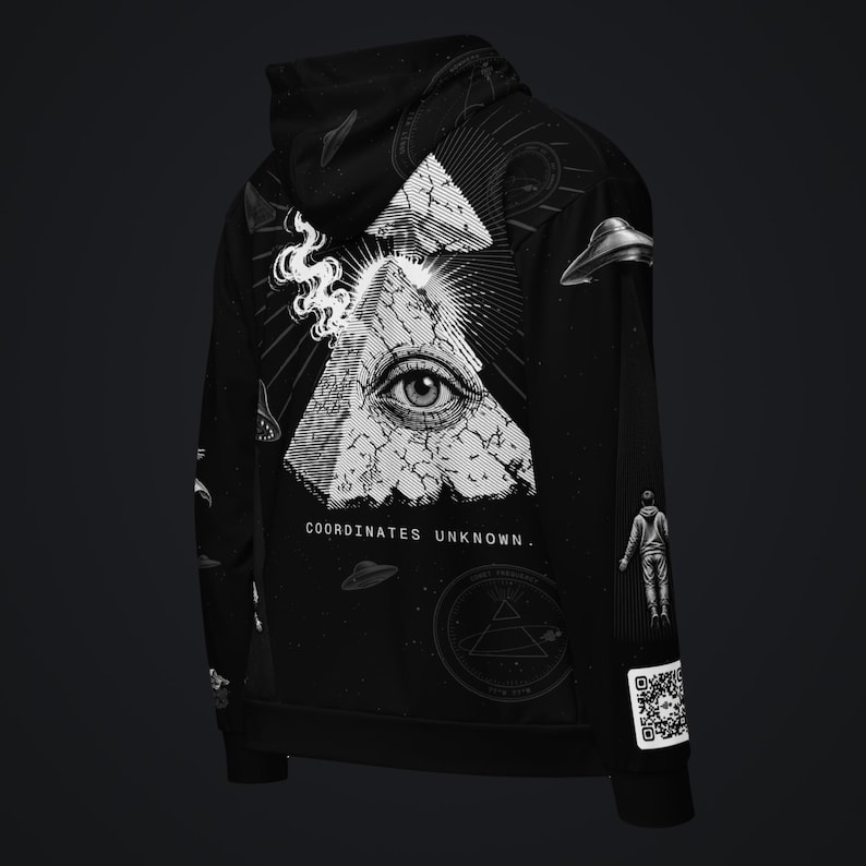 May include: A black hoodie featuring a white graphic of an eye inside a cracked pyramid, with smoke, UFOs, and a floating figure. The text "COORDINATES UNKNOWN." is printed below the pyramid, and a QR code is visible on the lower sleeve.